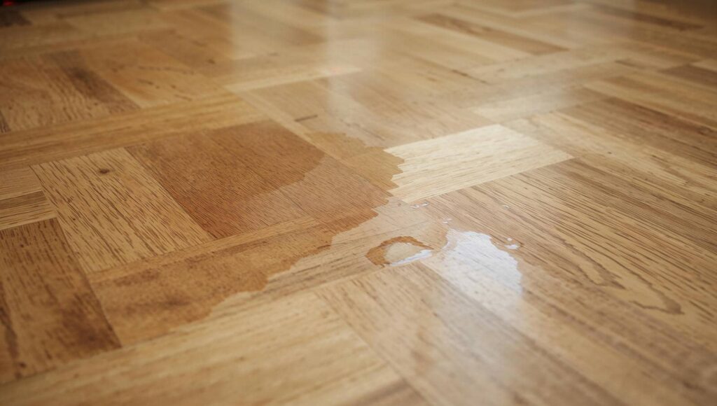 Water spilled on a wooden parquet floor creating a wet patch.